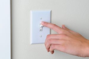 A light switch, and a finger poised to move the switch into the down position.