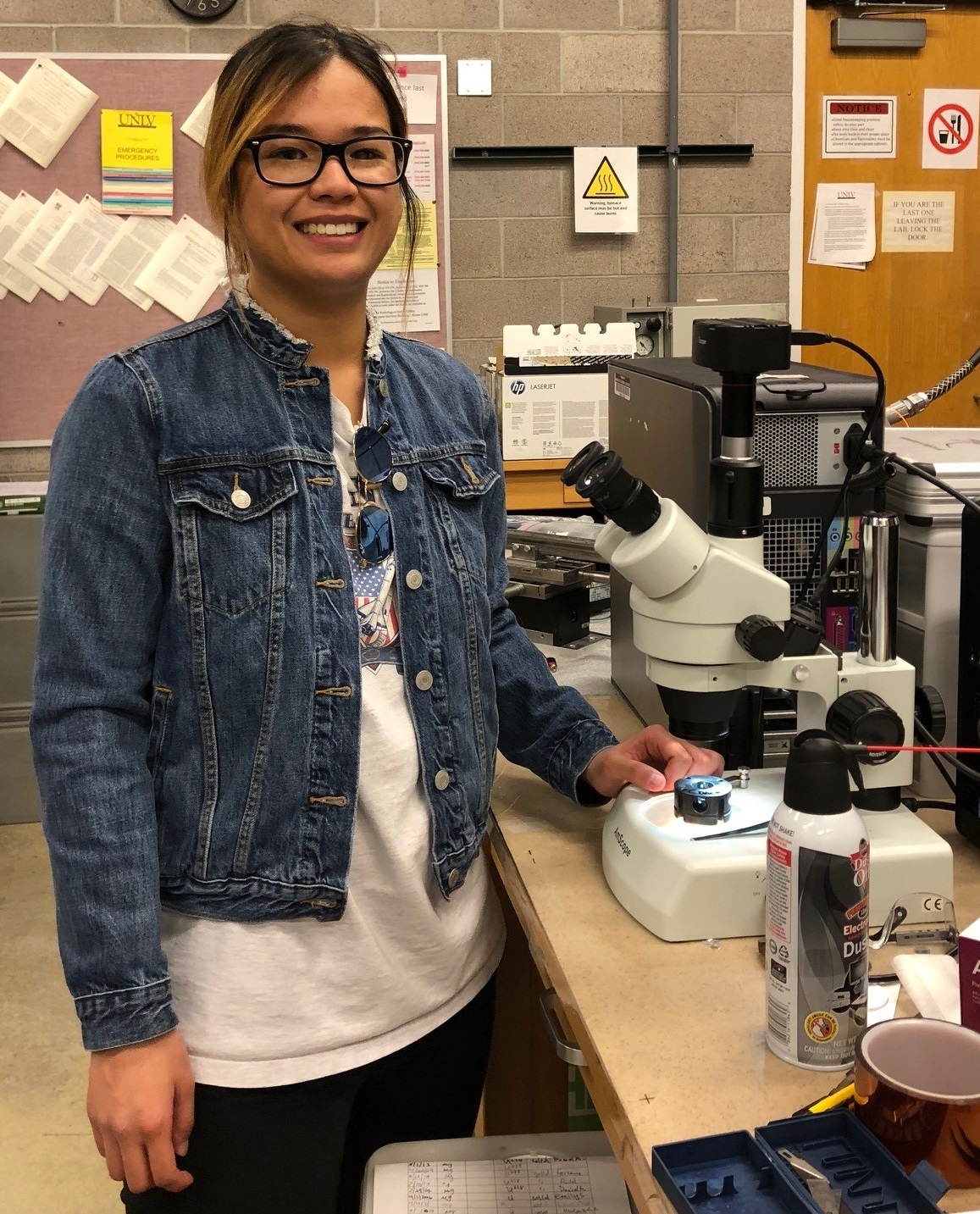 A UNLV student smiles for the camera beside a microscope