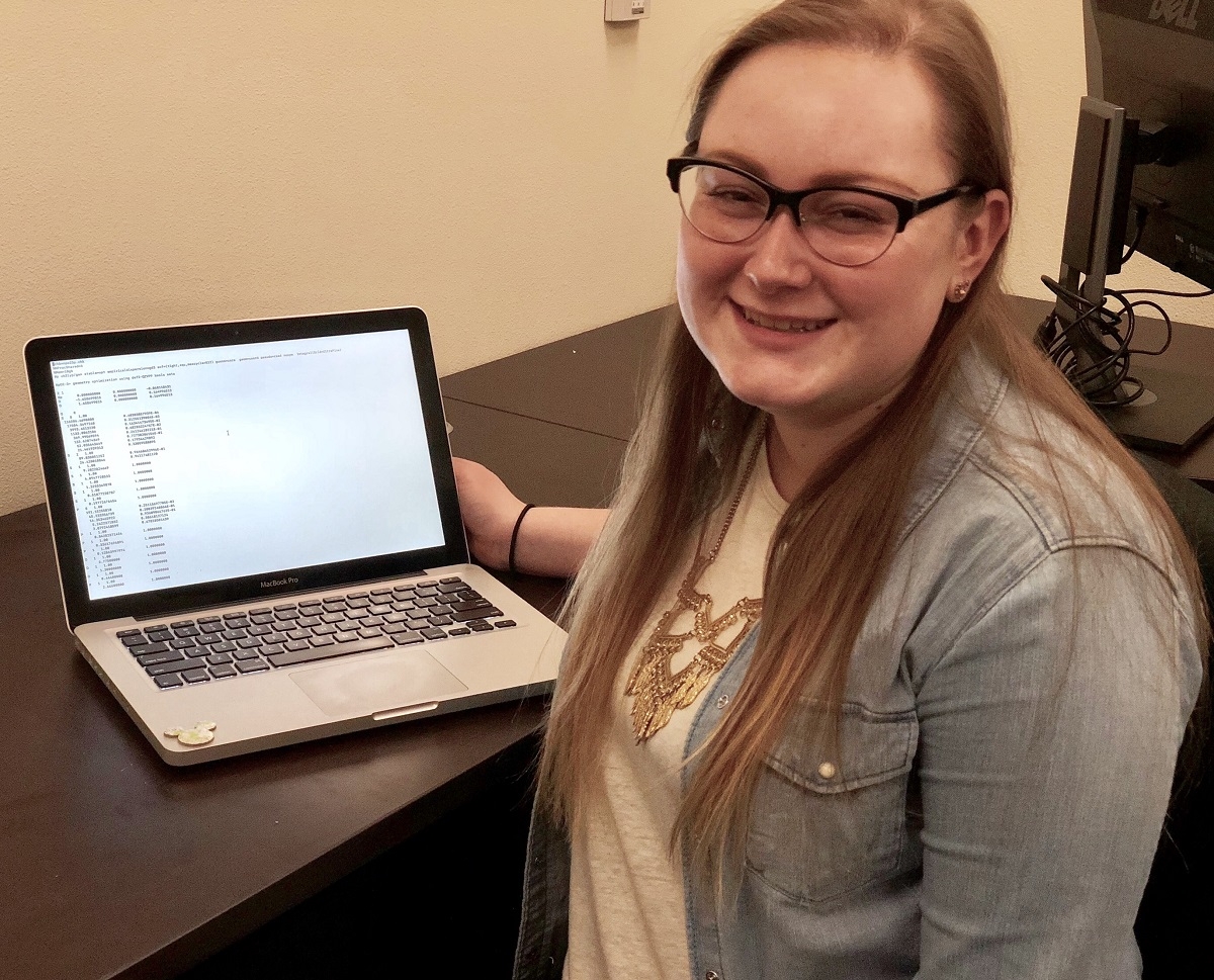 A UNR student smiles near a laptop running a scientific program