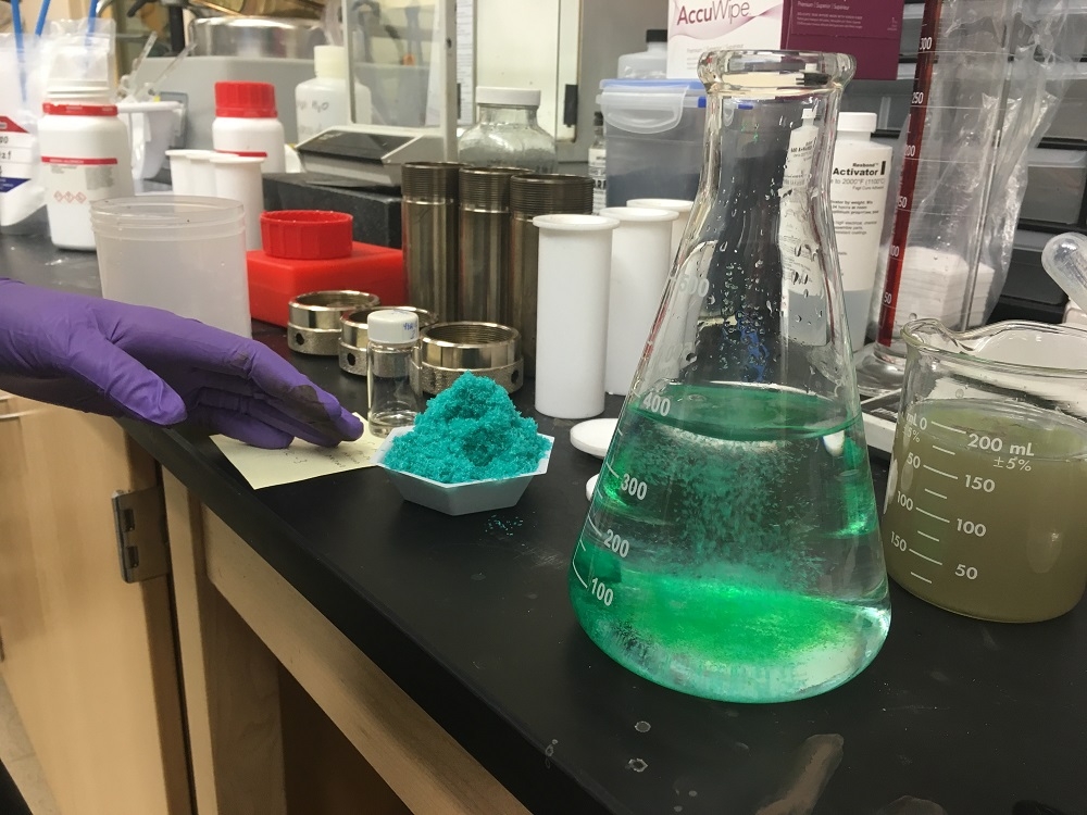 A scientific beaker holds a light green liquid compound